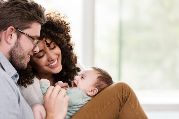 Adorable young family with newborn Happy young woman and her husband smile at their sweet newborn baby boy. They are relaxing in their home. two parents stock pictures, royalty-free photos & images