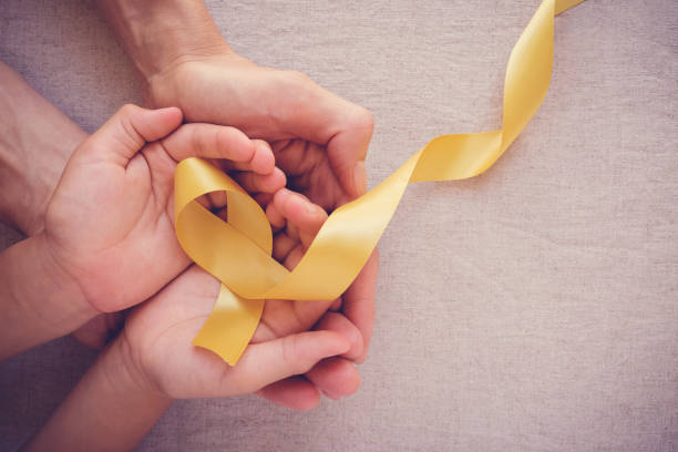adult and child hands holding yellow gold ribbon, Sarcoma Awareness, Bone cancer, childhood cancer awareness adult and child hands holding yellow gold ribbon, Sarcoma Awareness, Bone cancer, childhood cancer awareness children cancer stock pictures, royalty-free photos & images
