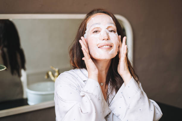 Adult brunette woman with sheet mask on her face in the bathroom at home stock photo