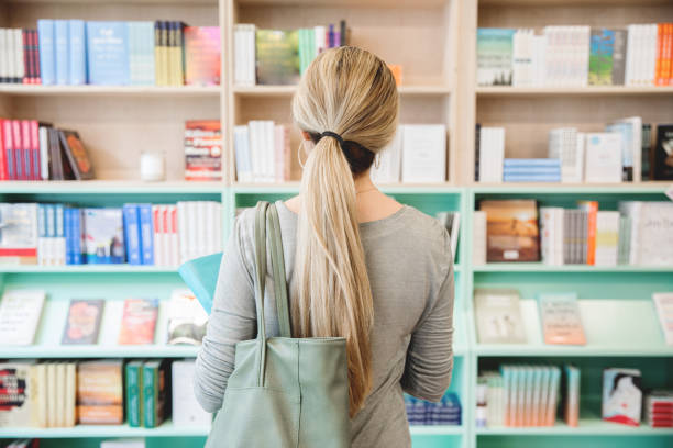 Adult female looking at books on the shelf in the bookstore stock photo