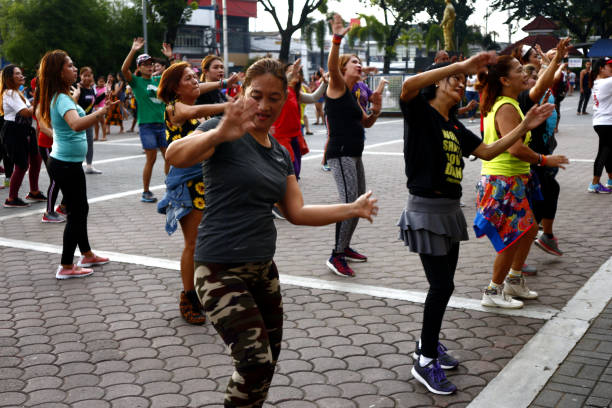 Adult Filipino ladies participate in a Zumba or dance exercise class at a public park. stock photo
