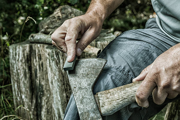 adult man hands sharpening rusty axe with whetstone - scherp stockfoto's en -beelden