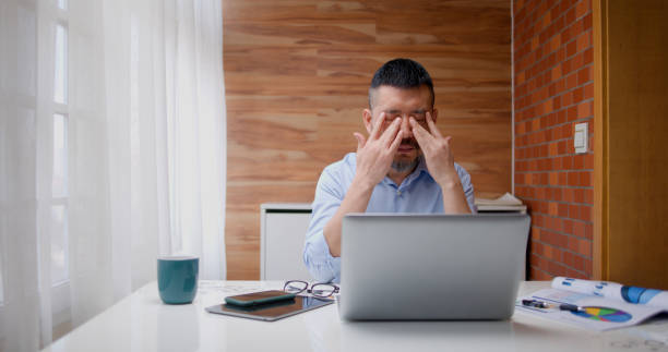 Adult man is tired and rubbing his eyes while working stock photo