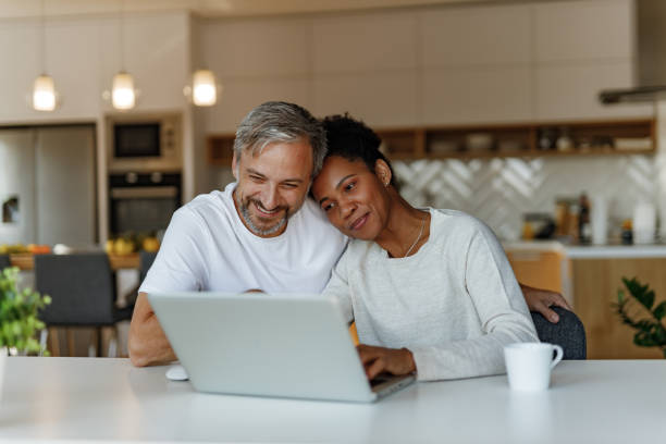 Adult people using laptop at home. Two lovers together looking their old photos and videos over the laptop. mature couple stock pictures, royalty-free photos & images