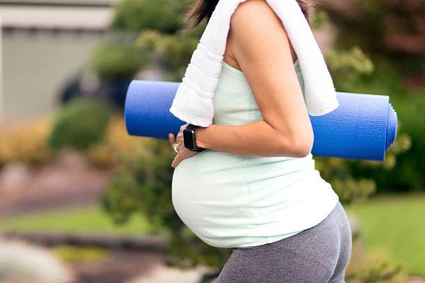 Adult pregnant woman carrying yoga mat and towel while outside  asian yoga pants stock pictures, royalty-free photos & images