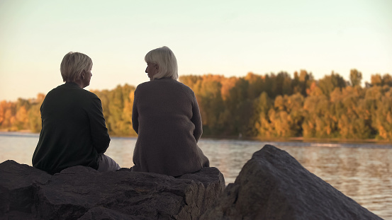 Adult women talking near lake in park, enjoying weekend outdoors, leisure