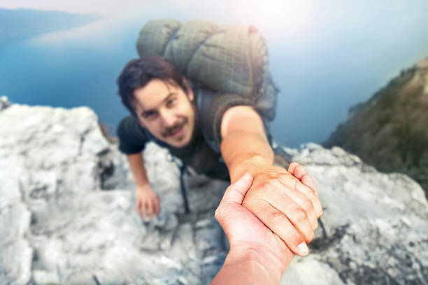 adventurers helping each other to climb the mountain stock photo