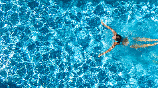 Aerial drone view of active girl in swimming pool from above, yong woman swims in blue water, tropical vacation, holiday on resort concept