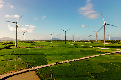 Aerial drone view of wind turbine tower farm in a big green meadow under the sunny sky generating renewable wind energy to support sustainable development and prevent environmental pollution