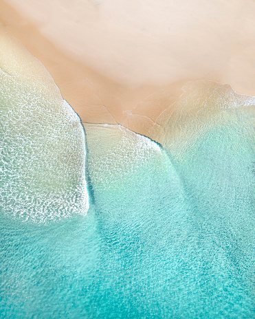Aerial of a beach with beautiful waves, white sand and ocean textures at sunrise