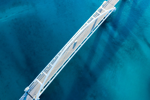 Clear ocean.\nViewpoint from directly above.\nThe shadow of the bridge appears on the surface of the water.