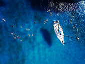 Aerial shot of beautiful blue lagoon at hot summer day with sailing boat. Top view of people are swimming around the boat.