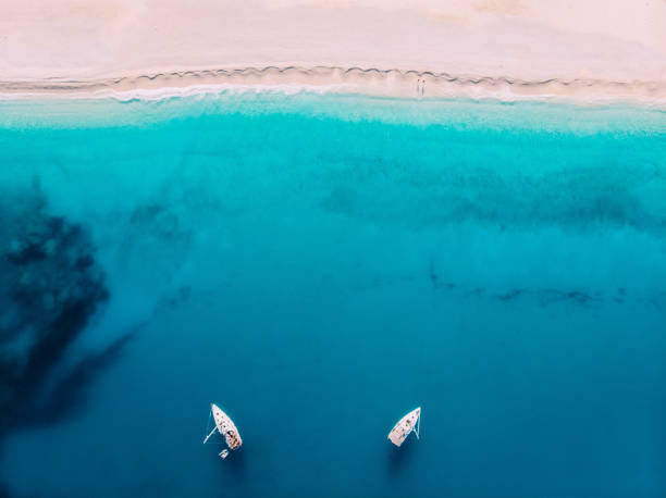 Aerial top down view two yachts stand at sea near white sandy beach stock photo
