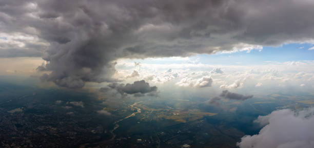 Aerial view from airplane window at high altitude of distant city covered with puffy cumulus clouds forming before rainstorm. stock photo