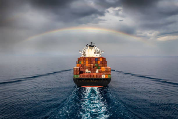 Aerial view of a container cargo ship sailing into bad weather Aerial view of a container cargo ship sailing into bad weather with a rainbow in the cloudy sky container ship stock pictures, royalty-free photos & images