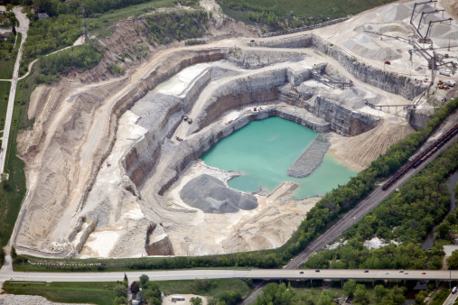 Aerial view of a large quarry site with a considerable amount of detail. Two mining trucks are climbing out of the pit, a large sorting and crushing operation is in the top right, a railroad runs down the right of the frame and a highway borders the bottom. Shot from the open window of a small airplane. http://www.banksphotos.com/LightboxBanners/Aerial.jpg