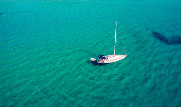 Aerial view of anchored sailing yacht in emerald sea. Aerial view of a boat. Outdoor water sports, yachting. Aerial view of anchoring yacht in open water. Ocean and sea travel and transportation Aerial view of anchored sailing yacht in emerald sea. Aerial view of a boat. Outdoor water sports, yachting. Aerial view of anchoring yacht in open water. Ocean and sea travel and transportation catamaran stock pictures, royalty-free photos & images