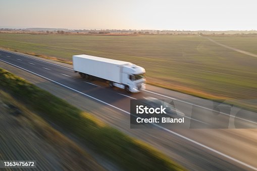 istock Aerial view of blurred fast moving semi-truck with cargo trailer driving on highway hauling goods in evening. Delivery transportation and logistics concept. Motion blurr effect 1363475672