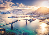 istock Aerial view of bridge, sea and snowy mountains in Lofoten Islands, Norway. Fredvang bridges at sunset in winter. Landscape with blue water, rocks in snow, road and sky with clouds. Top view from drone 1359901796