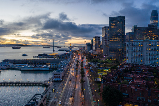 Aerial view looking down the Embarcadero in San Francisco as the sun is coming up. Ferry Building tower and early morning vehicles illuminate the road.