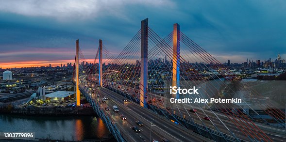 istock Aerial view of illuminated Kosciuszko Bridge at dusk, with the remote view of Manhattan and Brooklyn over the industrial zone of Williamsburg. High resolution stitched panorama. 1303779896