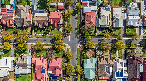 Aerial view of leafy eastern suburban houses on 4-way cross road intersection in Adelaide, South Australia: directly above, rooftop solar, trees in multiple colours (yellow, green, white); front & backyard, external garage, play equipment