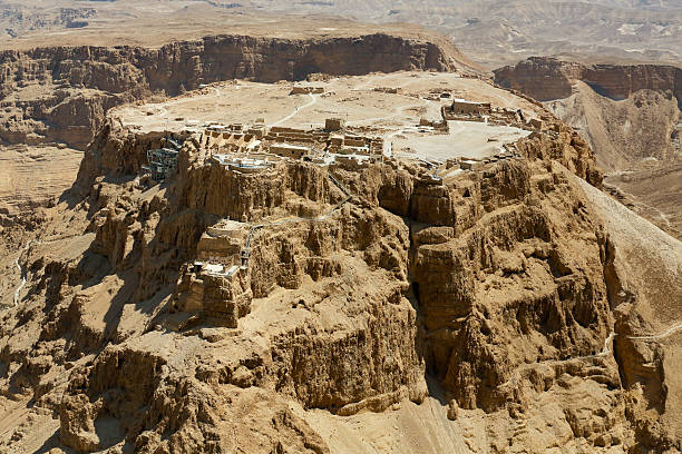 Aerial View of Masada Israel shot from a helicopter. Masada is an ancient fortification in the Southern District of Israel situated on top of an isolated rock plateau akin to a mesa on the eastern edge of the Judaean Desert, overlooking the Dead Sea. Herod the Great built palaces for himself on the mountain and fortified Masada between 37 and 31 BCE. According to Josephus, the Siege of Masada by troops of the Roman Empire towards the end of the First Jewish–Roman War ended in the mass suicide of the 960 Sicarii rebels and their families hiding there.