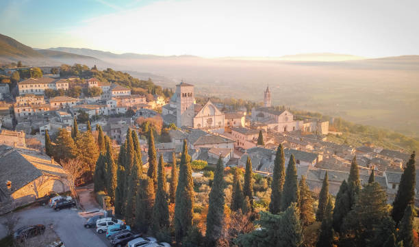 Aerial view of medieval city of Assisi bathed in evening sun with cypresses in foreground in Umbria, Italy stock photo