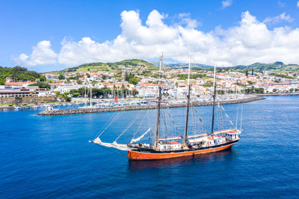 Aerial view of three masted schooner Sailing Vessel Buona Onda on roadstead, historical touristic hilly town centre and Marina da Horta full of luxury oceanic yachts stock photo