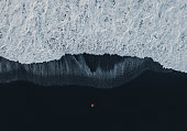 Aerial view of woman  in red coat standing on black sand beach in Iceland and looking at the sea