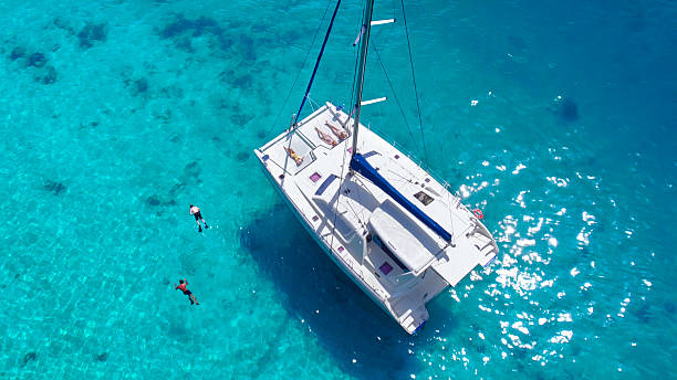Aerial view People relaxing on Catamaran anchored in tropical water Aerial view of people snorkeling and relaxing on a beatiful Catamaran anchored in clear tropical water in the Caribbean catamaran stock pictures, royalty-free photos & images