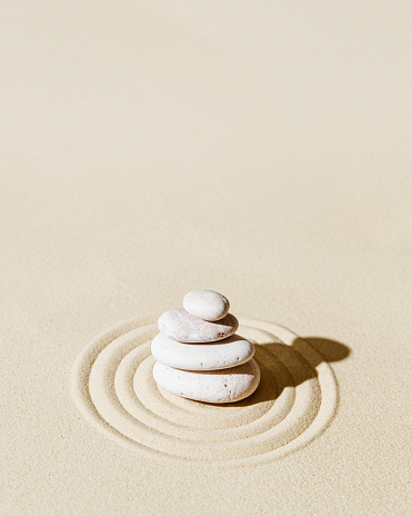 Aesthetic minimal background with zen stones on sand. Pattern in Japanese Zen Garden with concentric circles around white around stone cairn for meditation and tranquility.