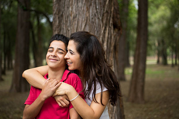 Affectionate latin mother embracing teen son and smiling An affectionate mature latin mother embracing her teen son and smiling in a horizontal waist up shot outdoors. mother and teenage son stock pictures, royalty-free photos & images