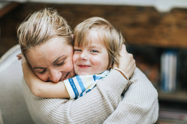 Affectionate mother and son embracing at home. Happy mother embracing her small son at home, while boy is looking at camera. close to stock pictures, royalty-free photos & images