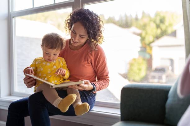 Affectionate mother reading book with adorable toddler daughter stock photo