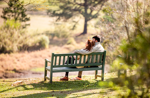 Affectionate young couple looking at the view while relaxing together on a bench in a park in spring