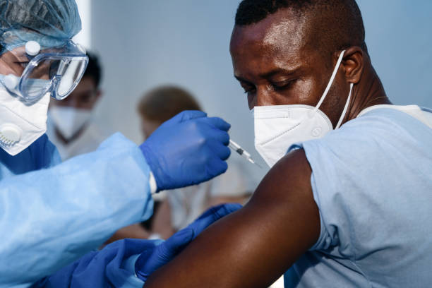 pria amerika afrika melihat jarum suntik virus corona covid-19 ketika staf medis menyuntikkan vaksin untuk mempersenjatai otot untuk membangun imunisasi virus corona covid-19 untuknya - konsep konsep & topik potret stok, foto, & gambar bebas royalti