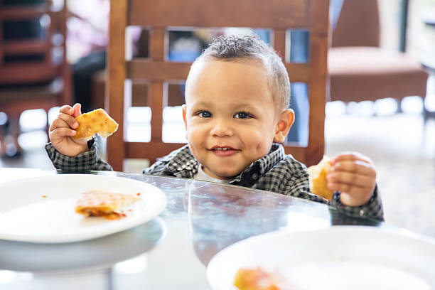 cậu bé người mỹ gốc phi ngồi tại bàn ăn ăn nhẹ - toddler eating hình ảnh sẵn có, bức ảnh & hình ảnh trả phí bản quyền một lần