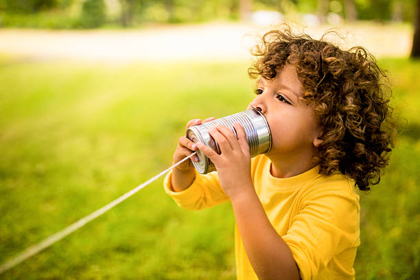 African American boy talking into tin can phone in park stock photo