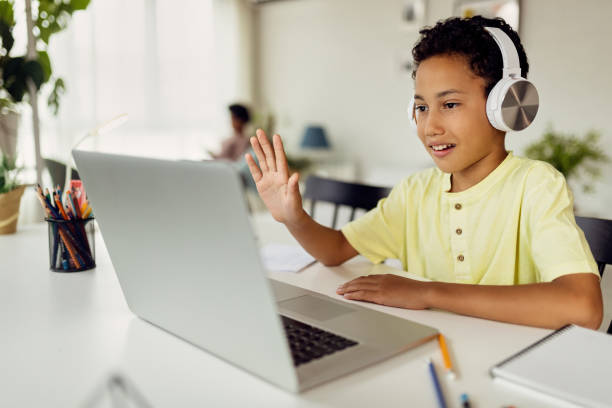 African American boy using laptop and waving during video call while homeschooling. Smiling black boy making video call over laptop and waving while e-learning at home. e learning stock pictures, royalty-free photos & images