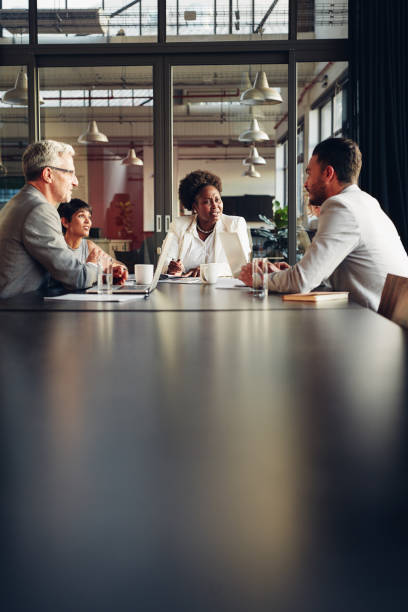 African American businesswoman listening to her team discussing work African American businesswoman sitting with her diverse team around a table in an office boardroom discussing work meeting room photos stock pictures, royalty-free photos & images