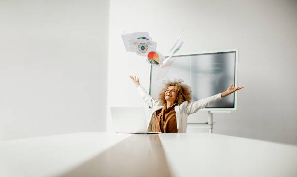 African American businesswoman throwing paper in the air after receiving of great news in the modern office stock photo