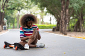 istock African American child girl fell to the ground while practicing skateboarding on the street in the park. 1338986025