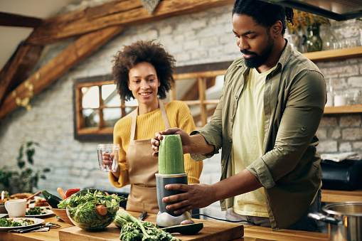 Black man blending healthy food while preparing smoothie with is wife in the kitchen.