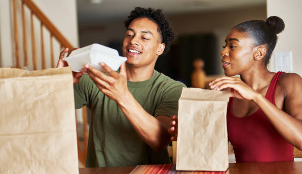 african american couple sitting at table looking at food delivery stock photo