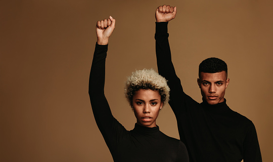 African american couple in black clothes standing supporting protests movement. Couple with raised fists symbolising fight against oppression.
