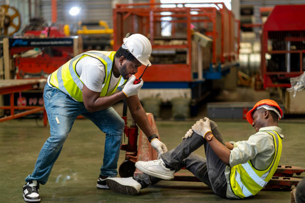 African American factory worker having accident while working in manufacturing site while his colleague is asking for first aid emergency team using walkie talkie radio for safety workplace concept stock photo