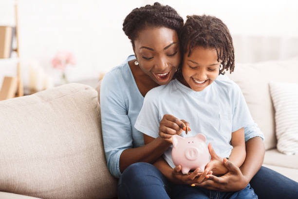 afrikaanse amerikaanse familie die geld in spaarvarken invoegt - sparen stockfoto's en -beelden