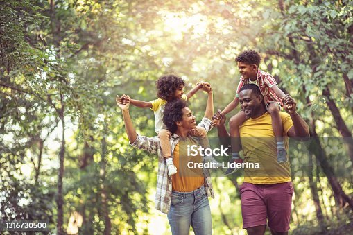istock African American family walking trough park. Parents carrying children on piggyback. 1316730500