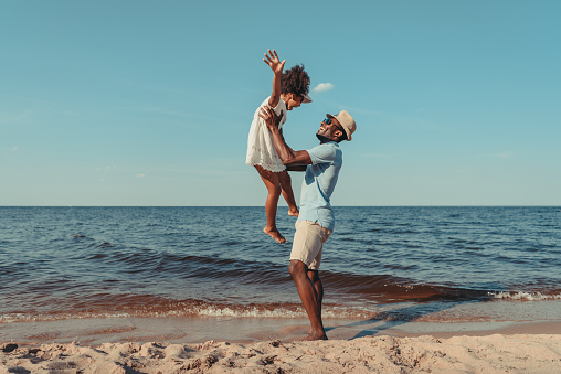 side view of happy african american father playing with cute little daughter on beach